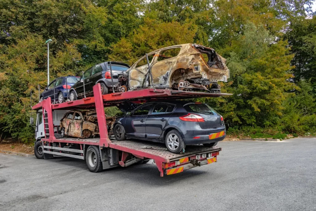 Autotransporter przewożący spalone i uszkodzone samochody, zaparkowany na tle drzew
