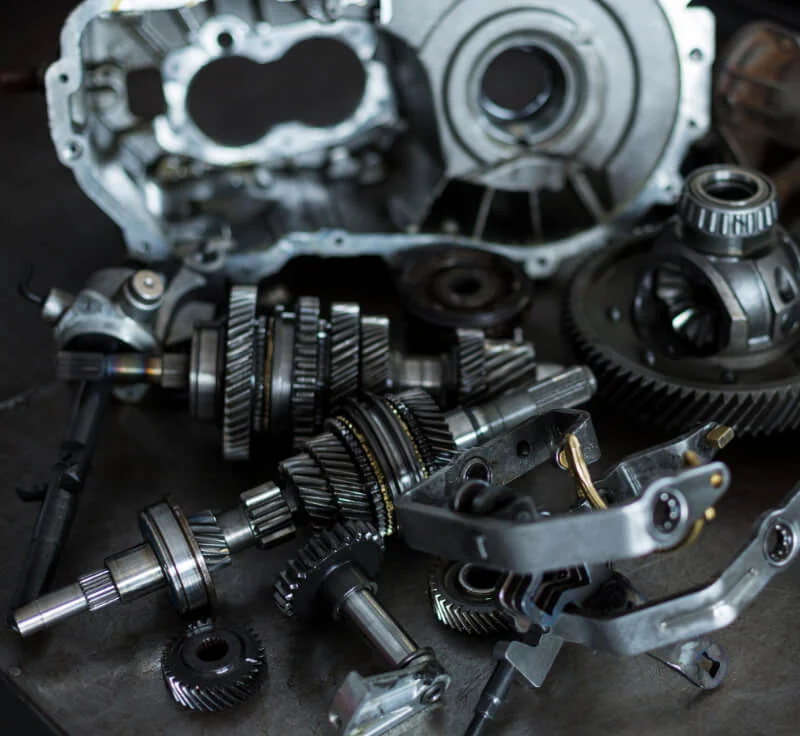 Rozebrana skrzynia biegów: koła zębate, wałki, mechanizm różnicowy i obudowa na ciemnym blacie